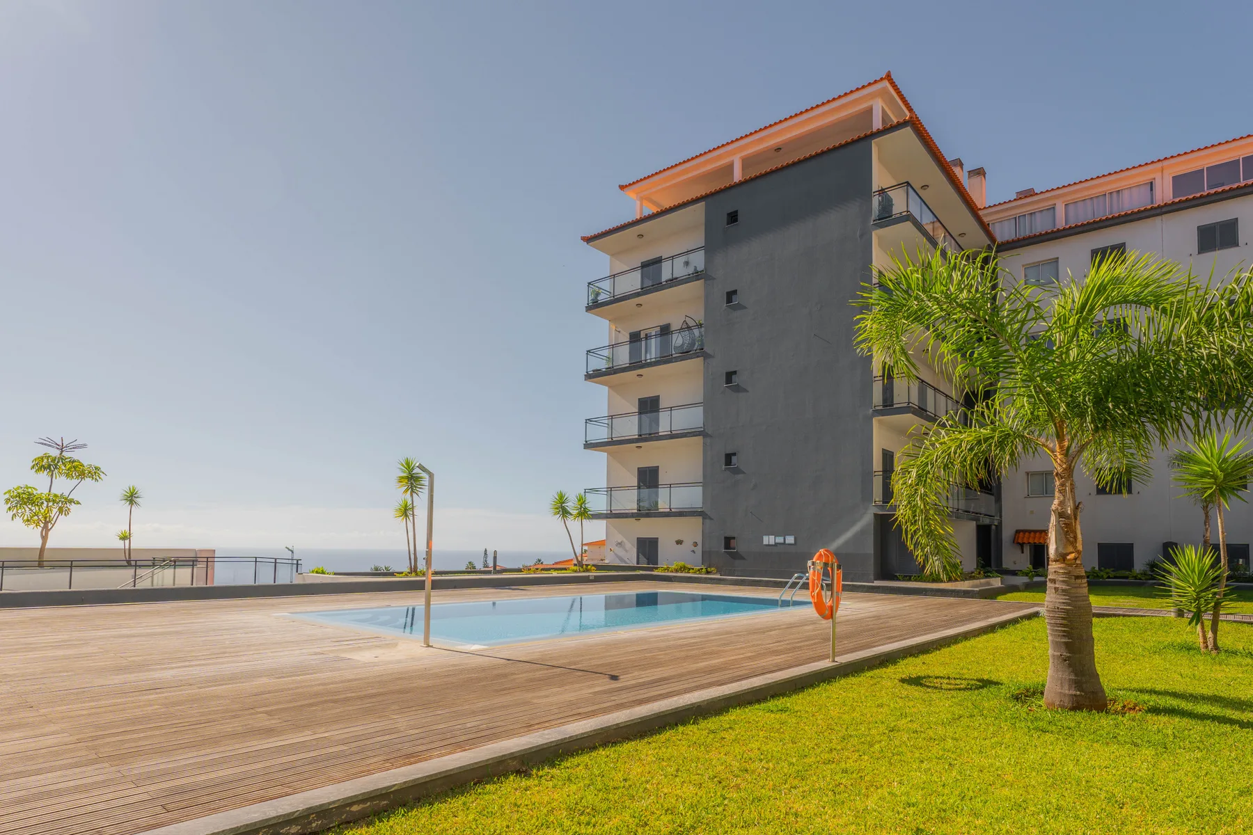 Un edificio moderno da a una piscina y jardines junto al océano.