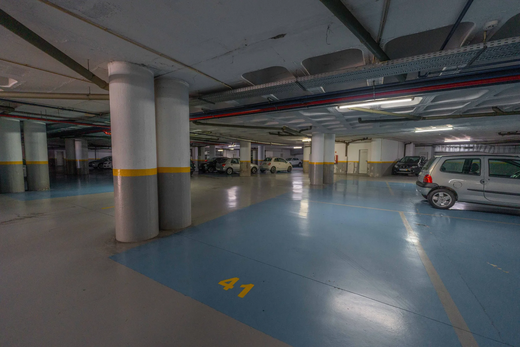 Un garaje cubierto con espacios señalizados y coches estacionados.