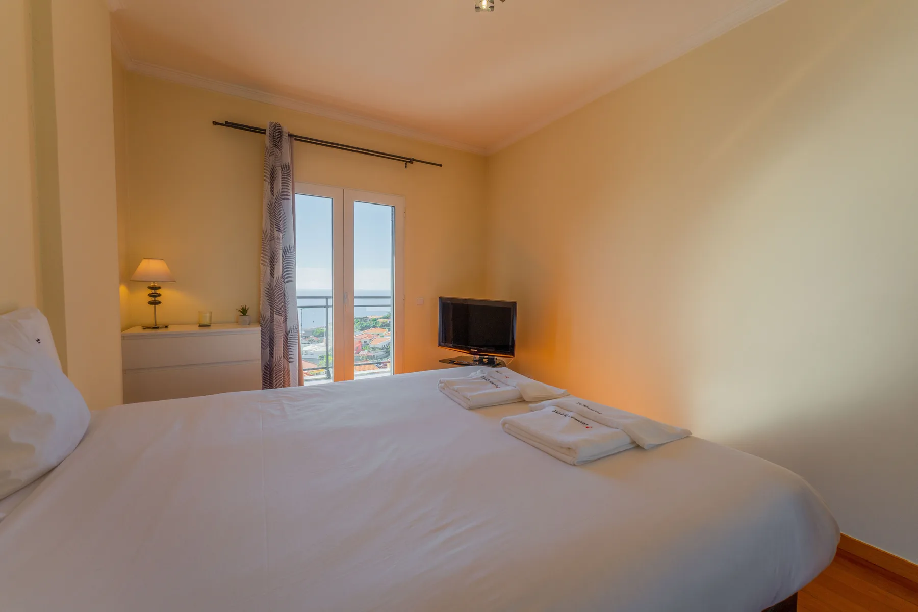Un dormitorio con una cama grande, un televisor y puertas de cristal que dan a un balcón.