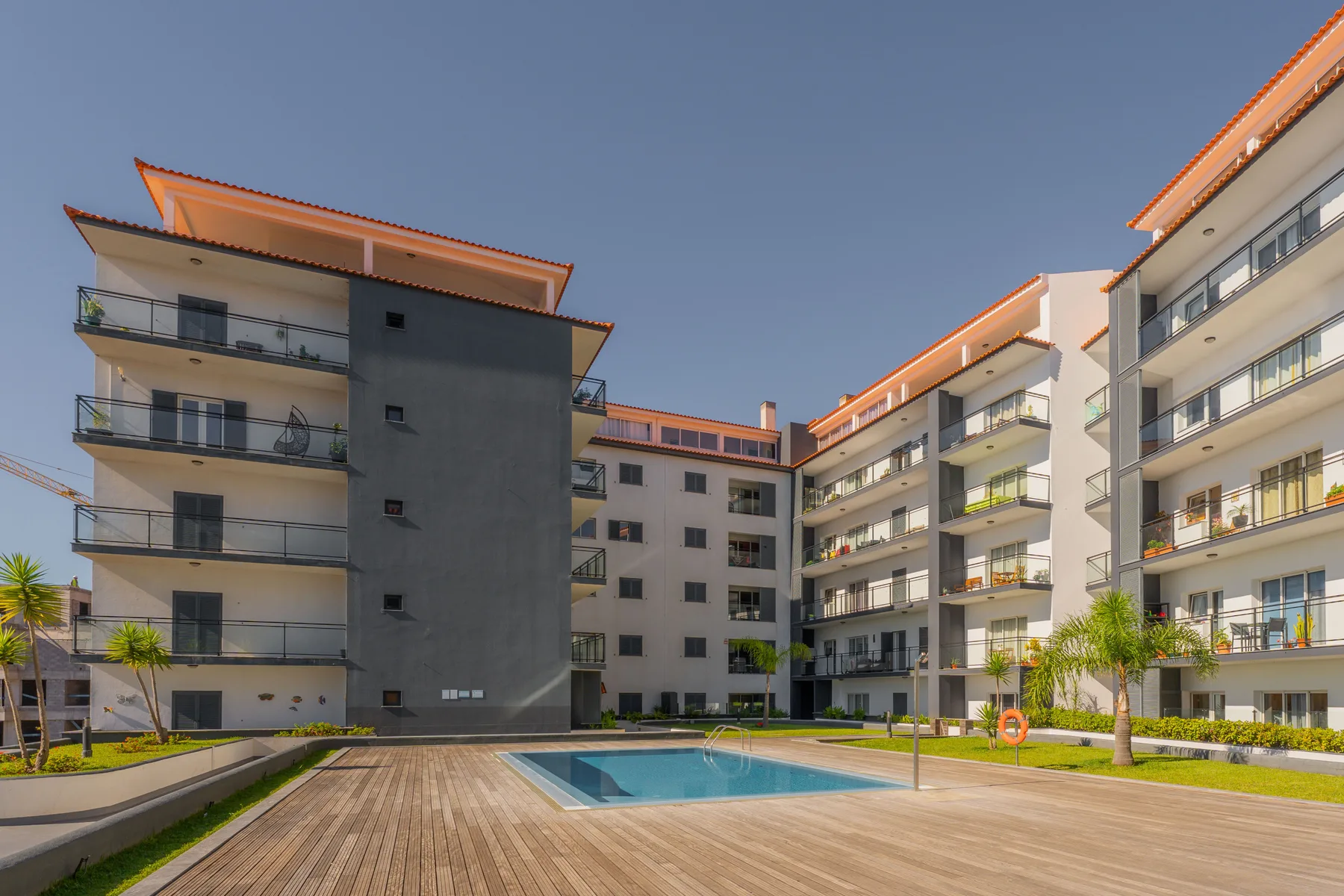 Edificios de apartamentos modernos rodean una piscina al aire libre y una terraza de madera.