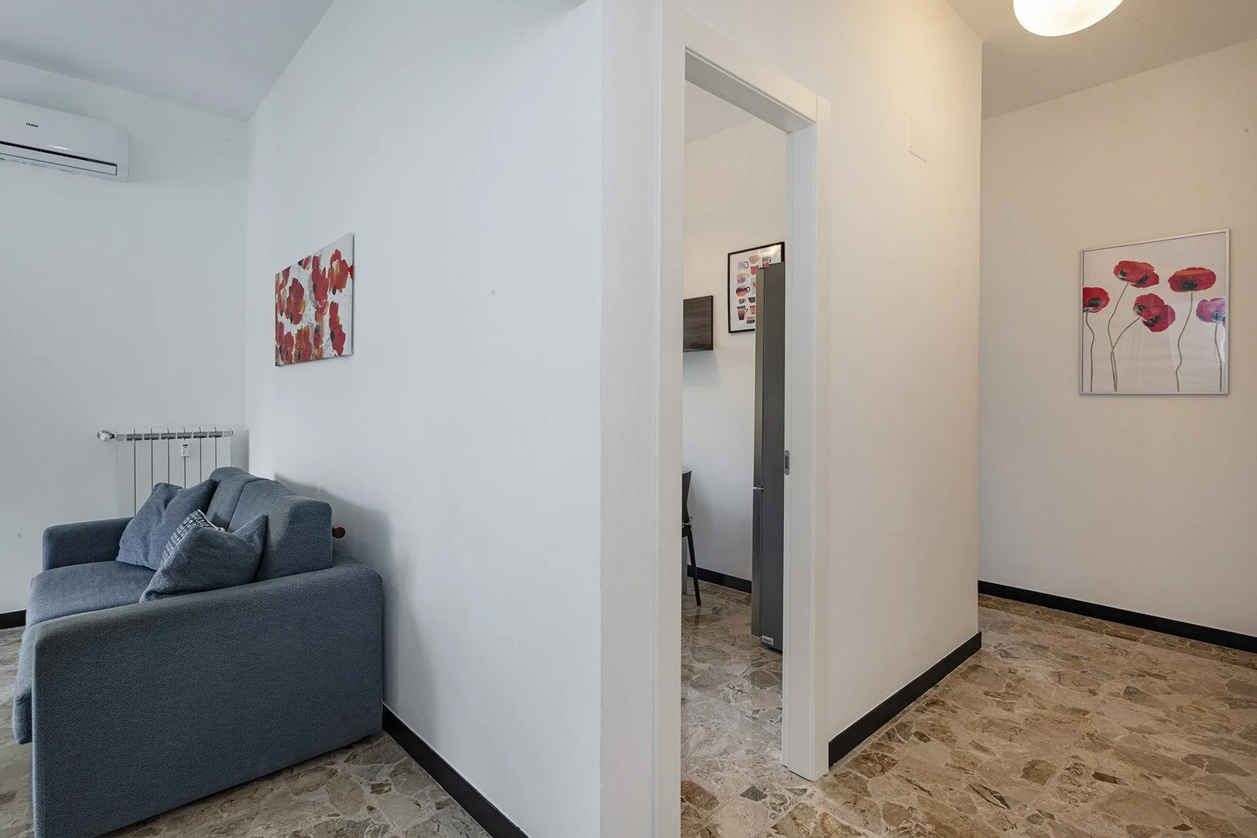 Una sala luminosa con asientos grises y cuadros florales junto a un pasillo.