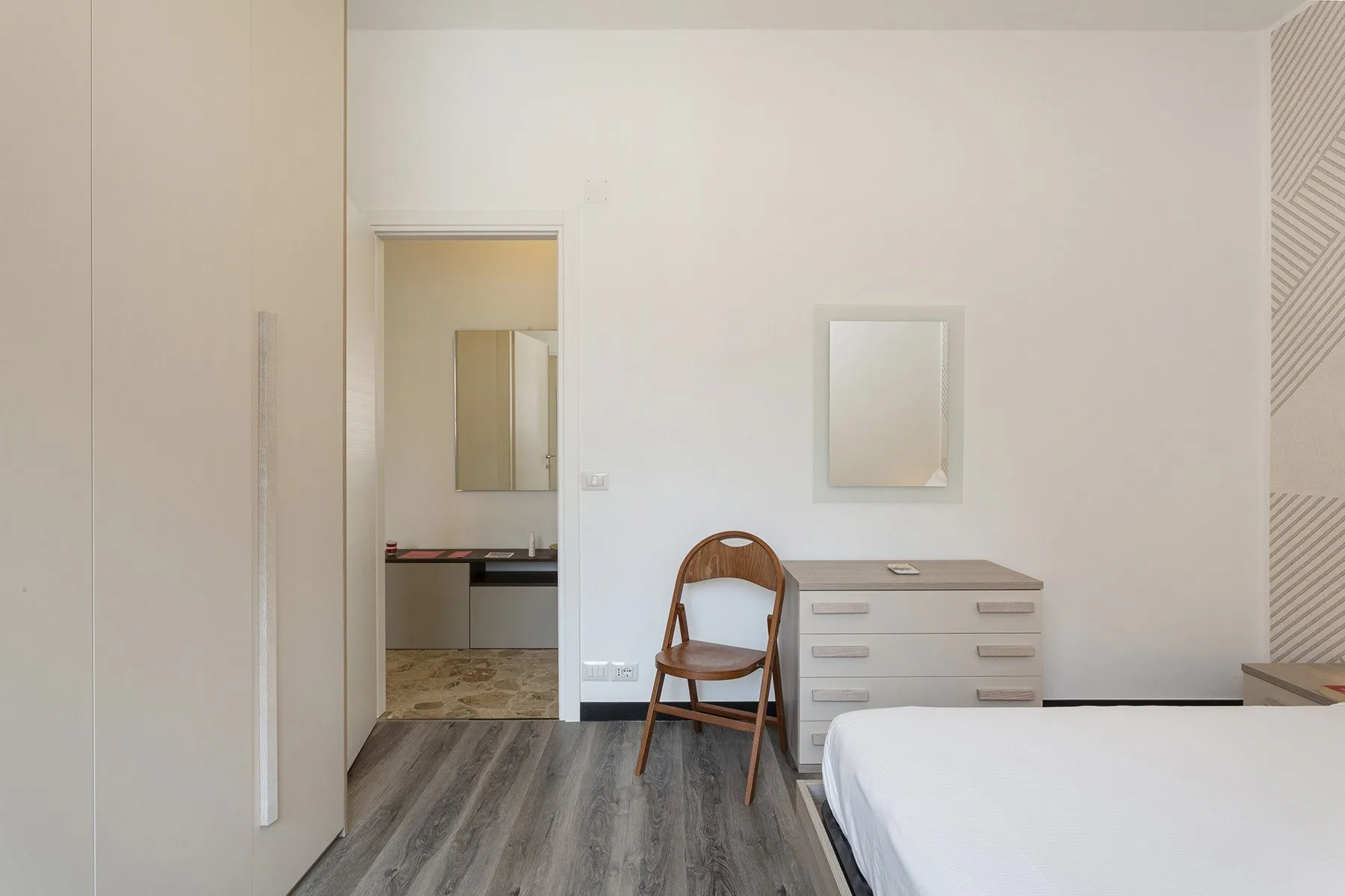 Un dormitorio luminoso con una cama, asiento de madera y cómoda.