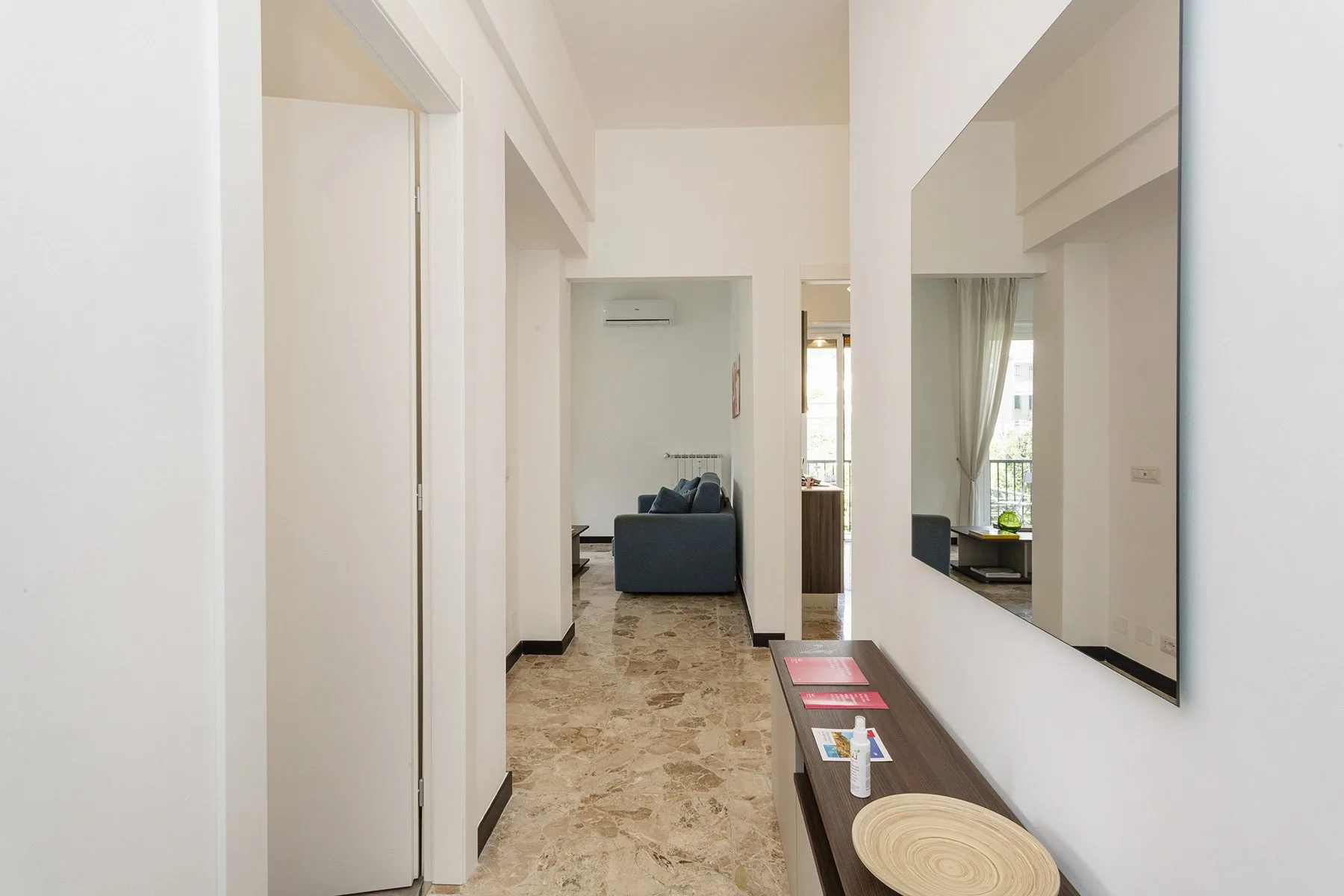 Un pasillo luminoso conduce a una sala de estar, con una consola y un espejo.