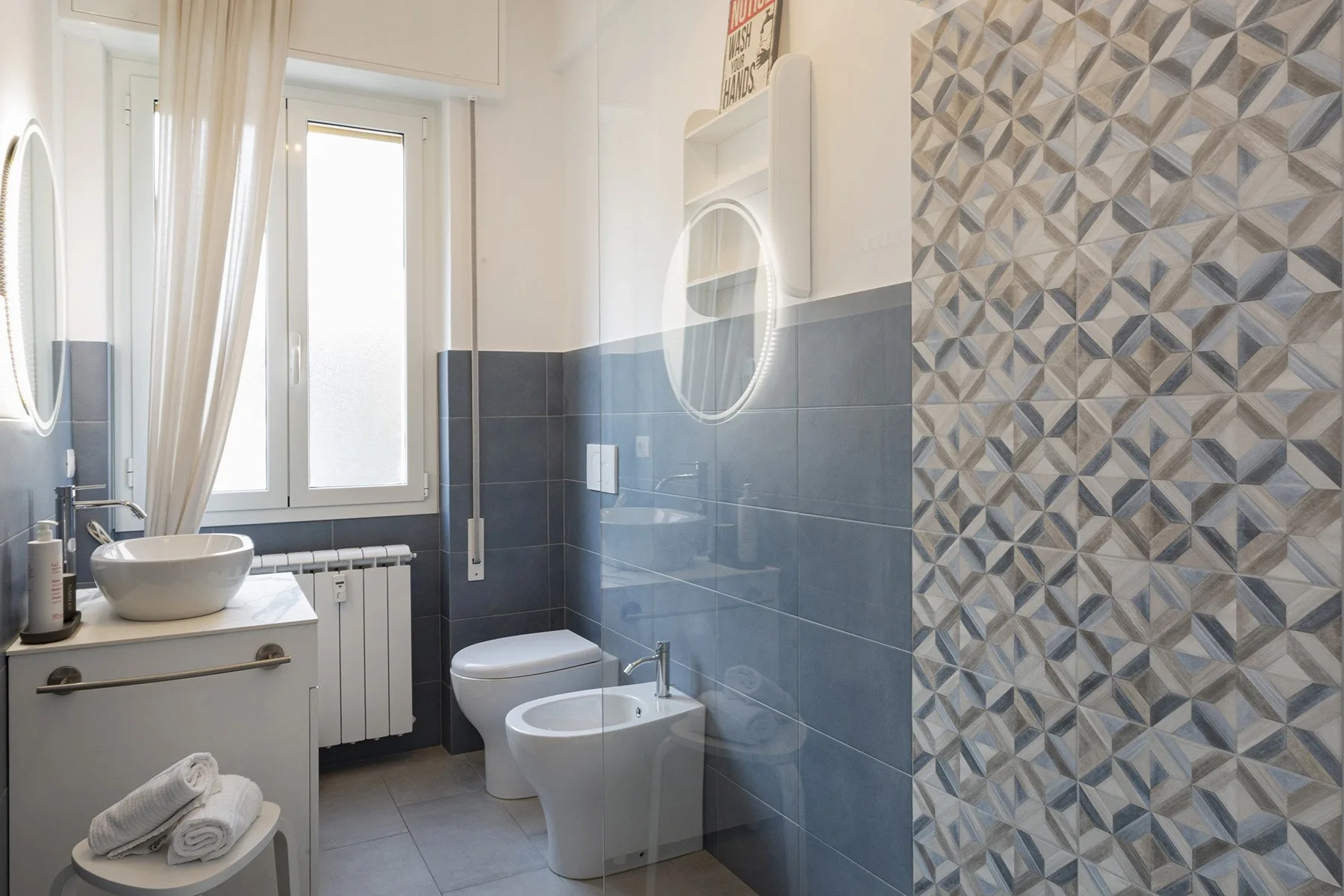 Un baño con lavabo, inodoro, bidé y azulejos estampados en la pared.