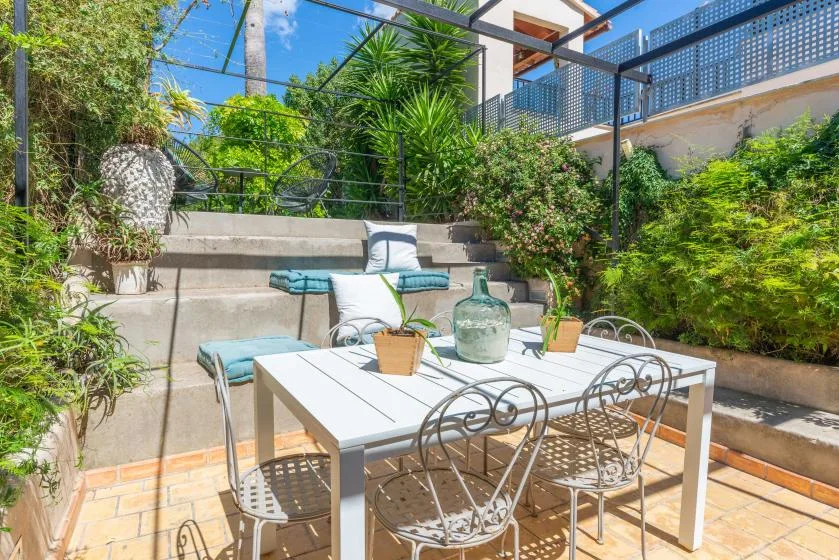 Un patio al aire libre con una mesa blanca y vegetación alrededor.