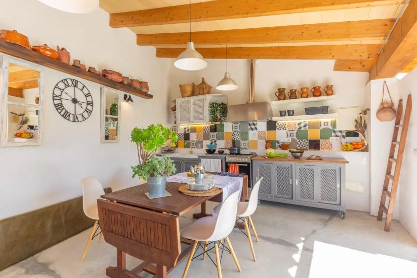 Una cocina luminosa con zona de comedor y una mesa de madera bajo vigas vistas.