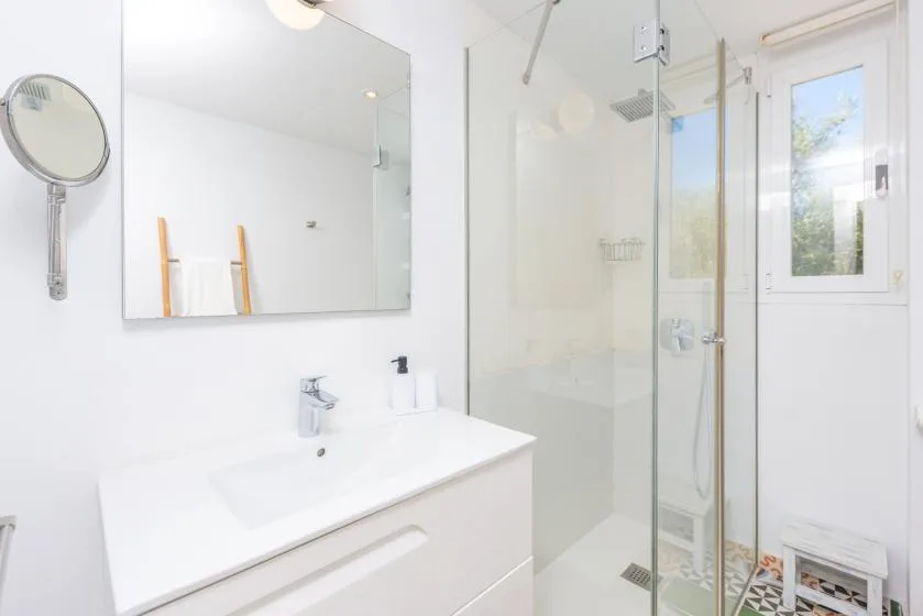 Un baño luminoso con lavabo, espejo y ducha de vidrio.