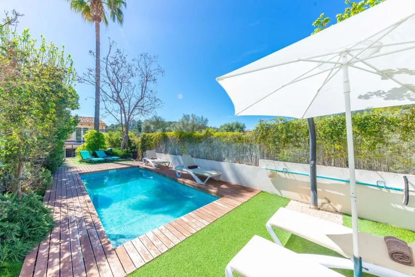 Una zona de piscina al aire libre con tumbonas, vegetación y una gran sombrilla blanca.