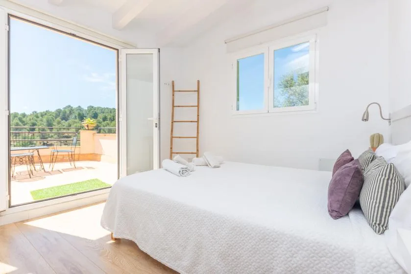 Un dormitorio luminoso con una cama bien tendida junto a puertas abiertas a un balcón.