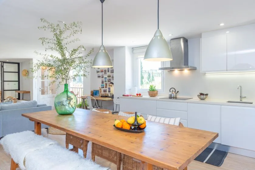 Una cocina y comedor de concepto abierto con una mesa de madera y gabinetes blancos.