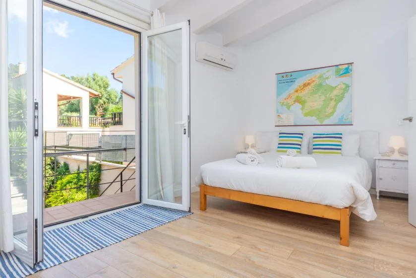 Un dormitorio luminoso con una cama y puertas abiertas que dan a un balcón.
