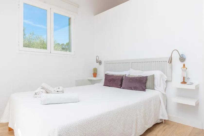 Un dormitorio luminoso con una cama bien tendida y una ventana con vistas a la vegetación.