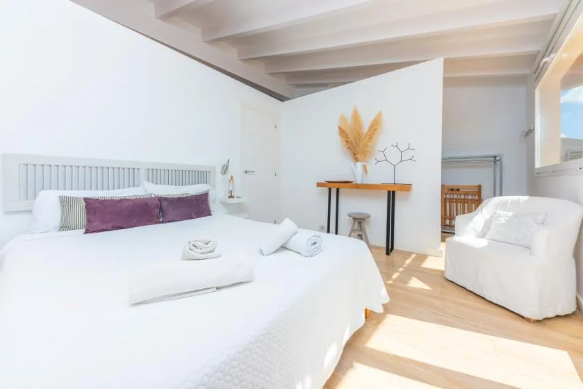 Un dormitorio luminoso con una cama grande y un sillón blanco.
