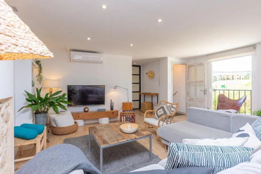 Una sala luminosa con asientos, una mesa de centro y la puerta del balcón abierta.