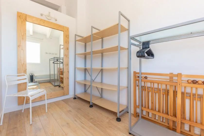 Una habitación luminosa con estantes abiertos, un espejo de cuerpo entero y una cuna de madera.