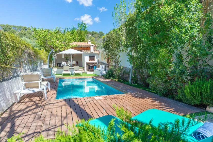 Una piscina al aire libre está junto a una terraza de madera, con asientos y árboles cerca.