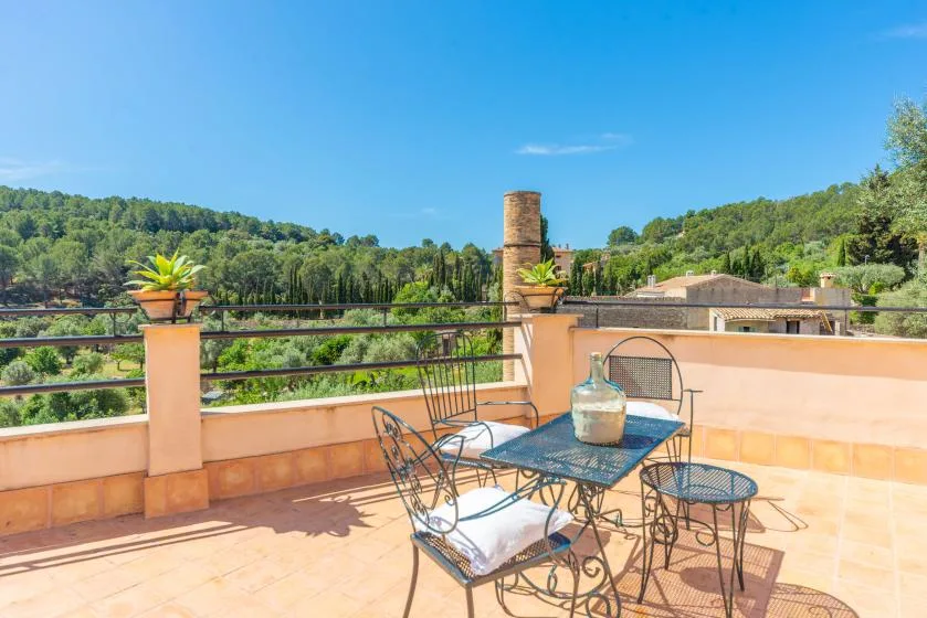 Una terraza soleada tiene una mesa metálica y asientos con vistas a colinas verdes.