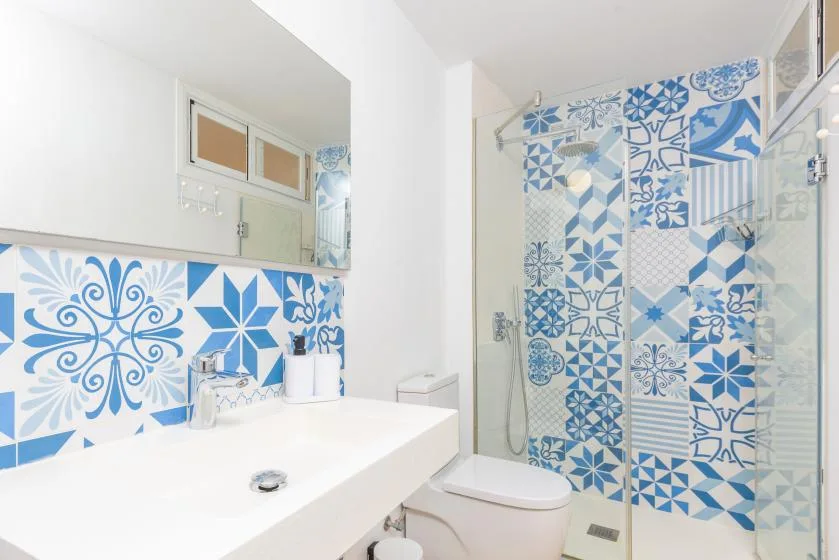 Un baño luminoso con un lavabo blanco y una zona de ducha con diseños azules.
