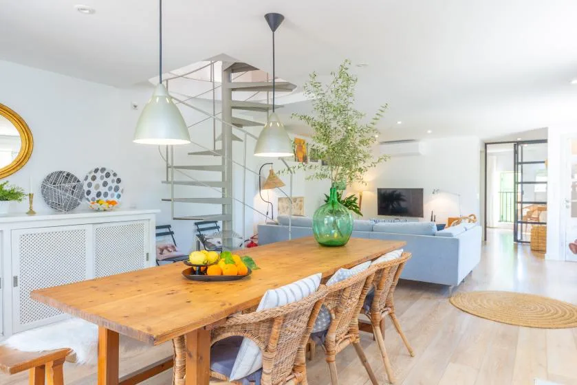 Una luminosa sala-comedor diáfana tiene una mesa de madera y asientos.