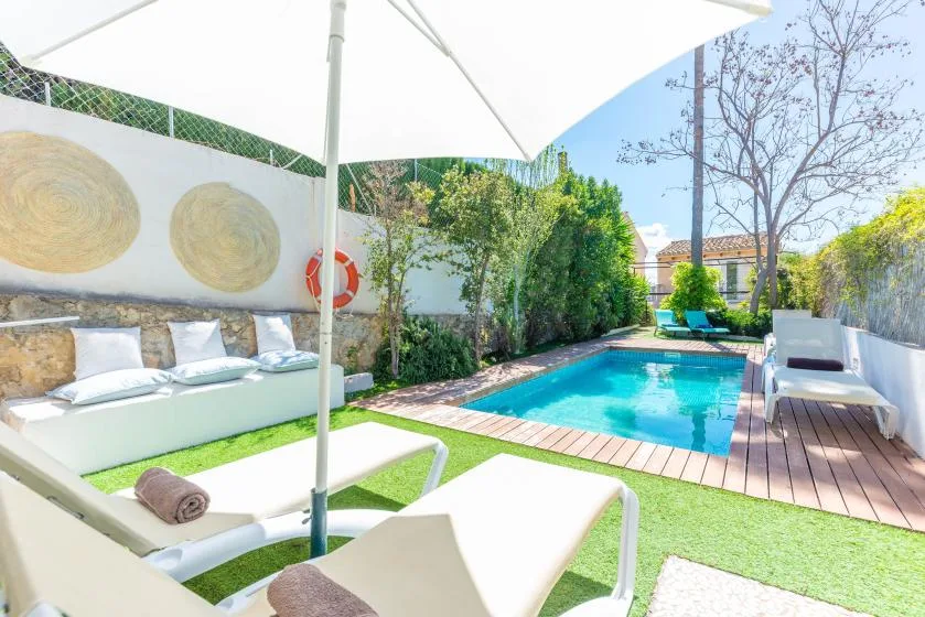Una piscina al aire libre está rodeada de asientos reclinables y vegetación.
