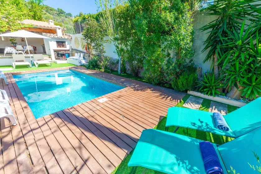 Una piscina junto a una terraza de madera y asientos turquesa.