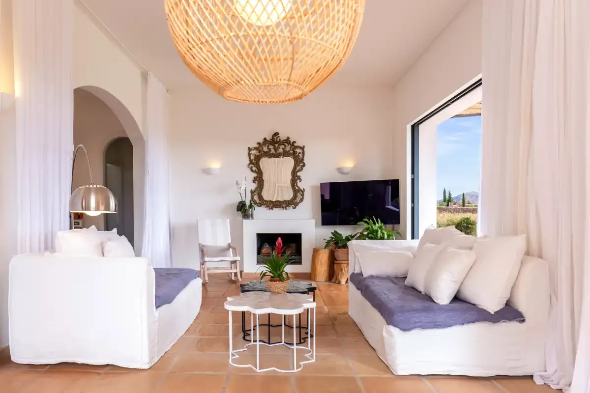 A bright living room with white seating, a fireplace, and a large woven pendant light.