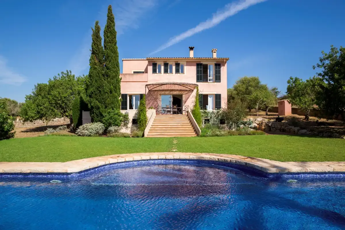 A pink house stands behind a swimming pool and a broad green lawn.