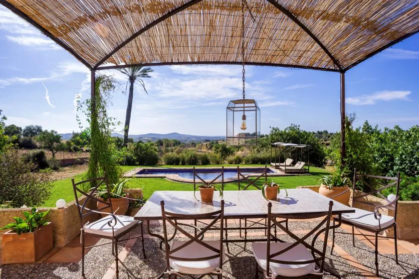 An outdoor dining area under a shaded canopy overlooks a garden pool.