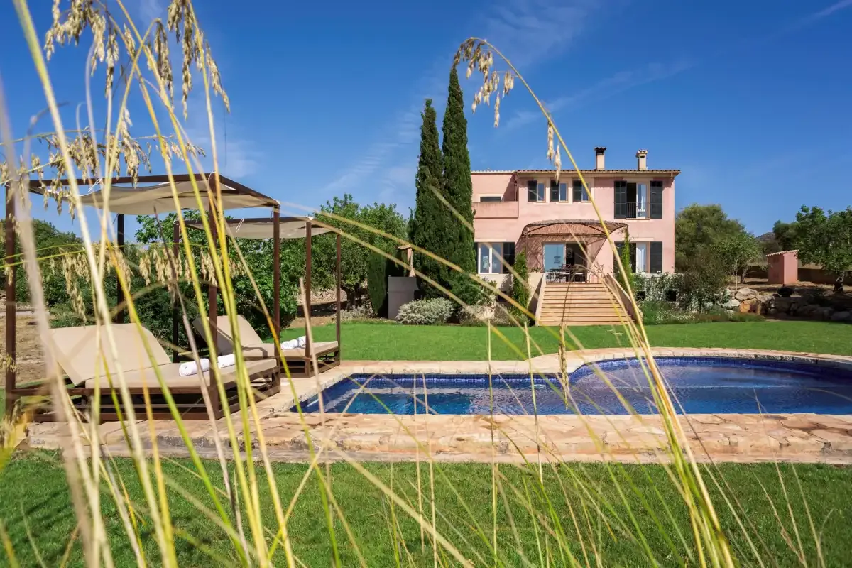 A pink house overlooks a swimming pool and landscaped garden.