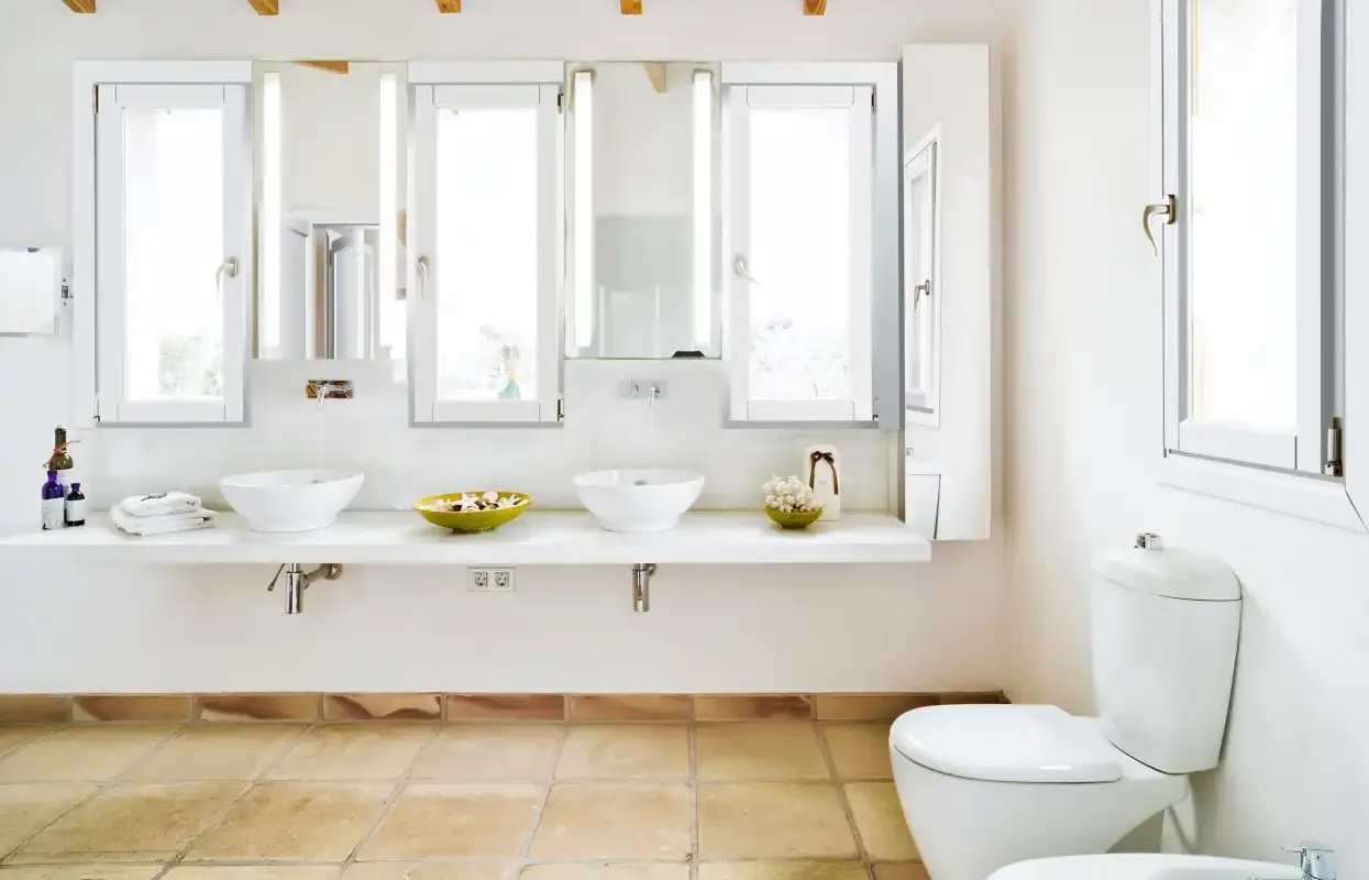 A bright bathroom with a long vanity, two sinks, and a toilet.