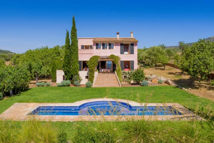 A two-story house and swimming pool sit amid green lawns and trees.