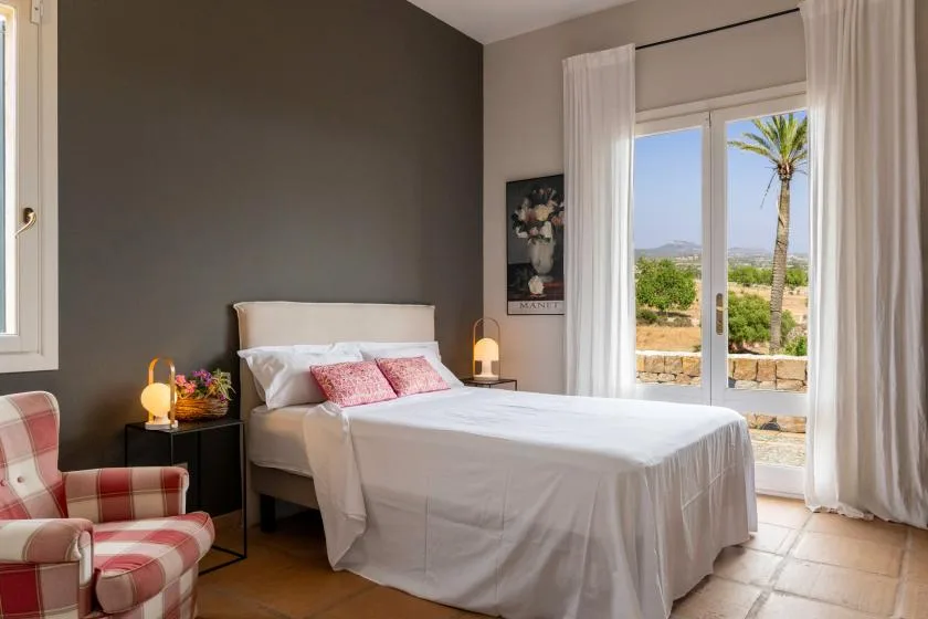 A bedroom with a neatly made bed, bedside tables, and a bright glass door.