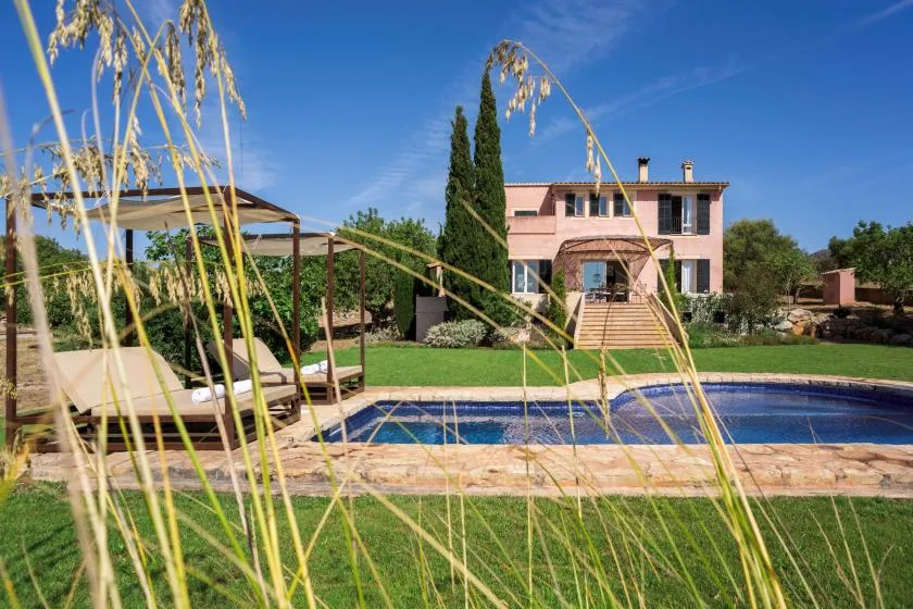 A swimming pool and landscaped garden sit in front of a pink house.