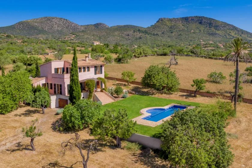 A countryside villa overlooks a green lawn and swimming pool, with hills in the distance.