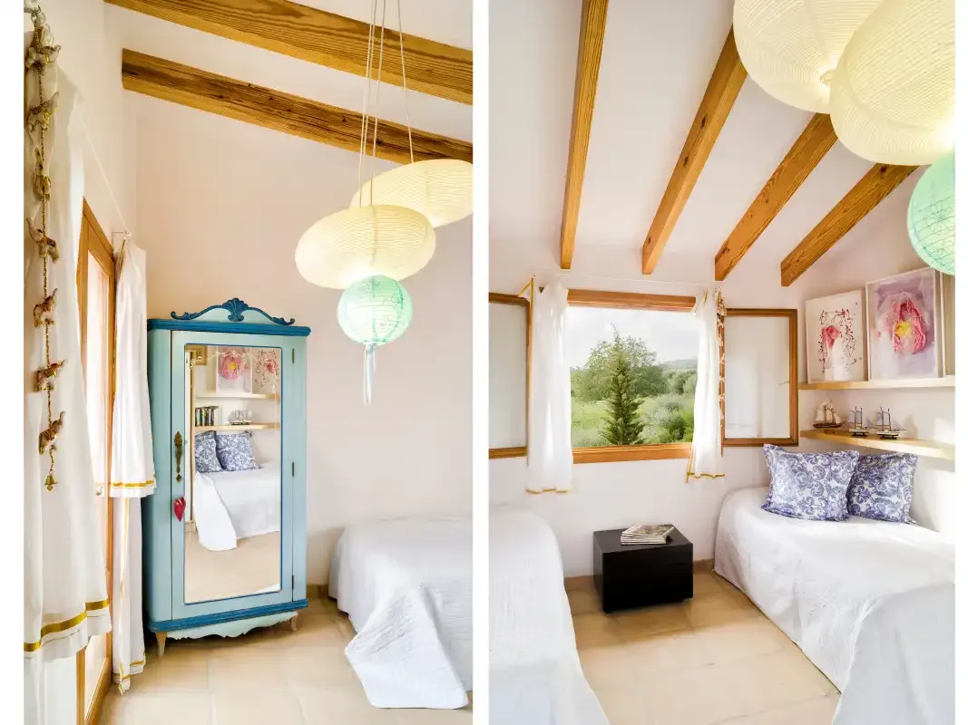 A bright bedroom with white bedding, exposed wooden beams, and hanging paper lamps.