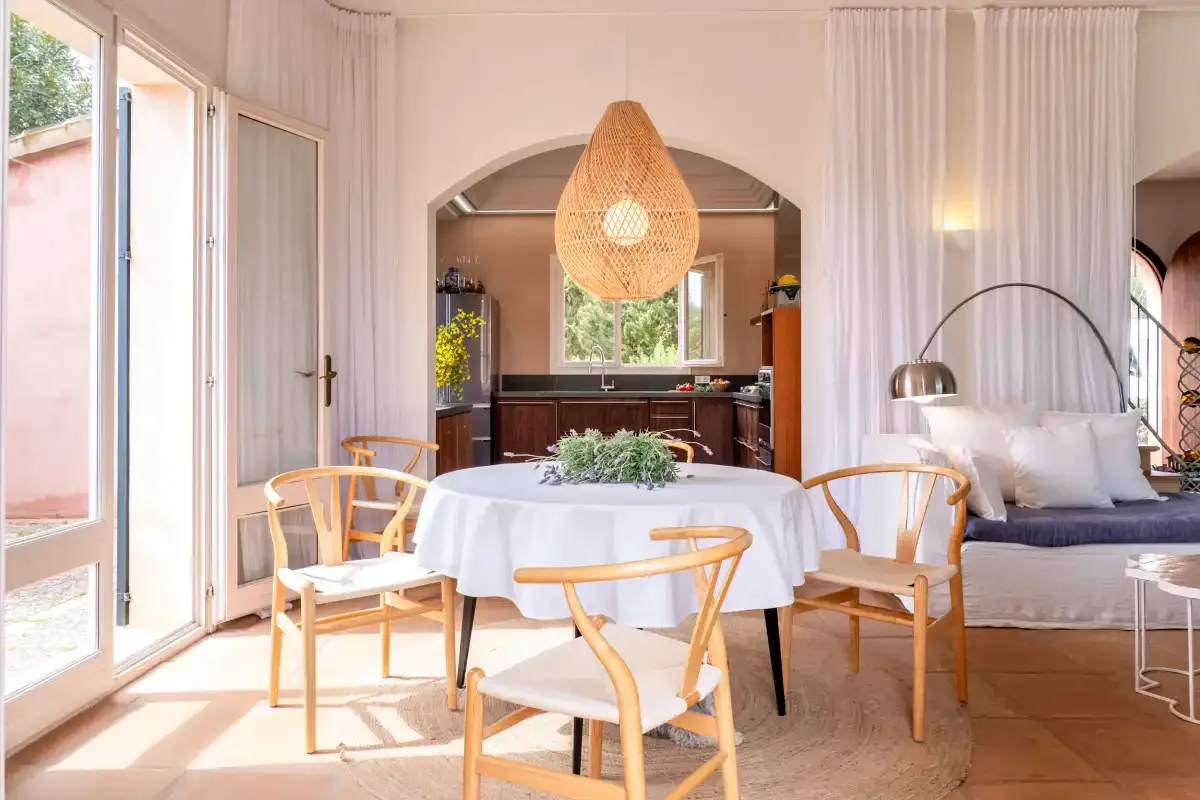 A dining area with a round table and chairs, opening onto a kitchen and seating area.