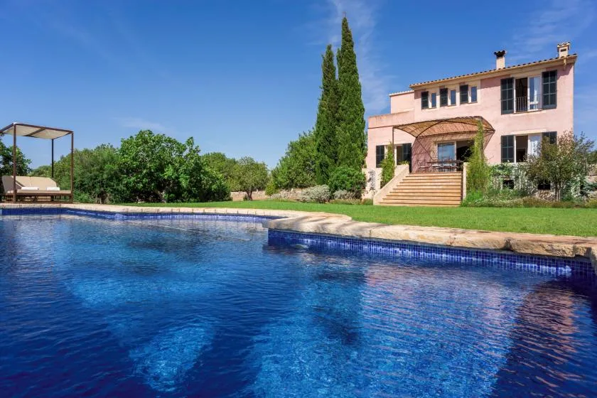 A swimming pool in front of a two-story house and landscaped garden.
