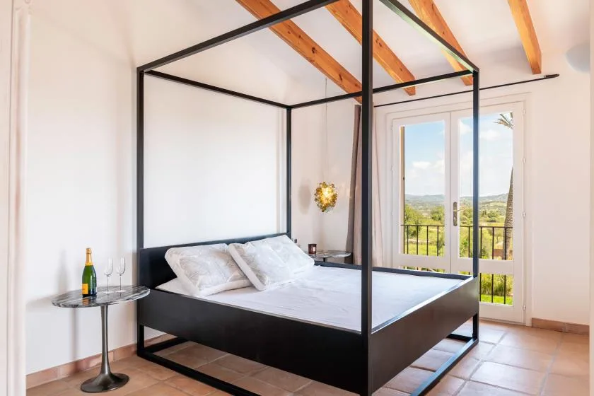 A bedroom with a black four-poster bed and glass doors opening onto a balcony.
