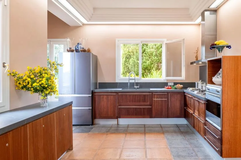 A bright kitchen with wooden cabinets and a window overlooking greenery.