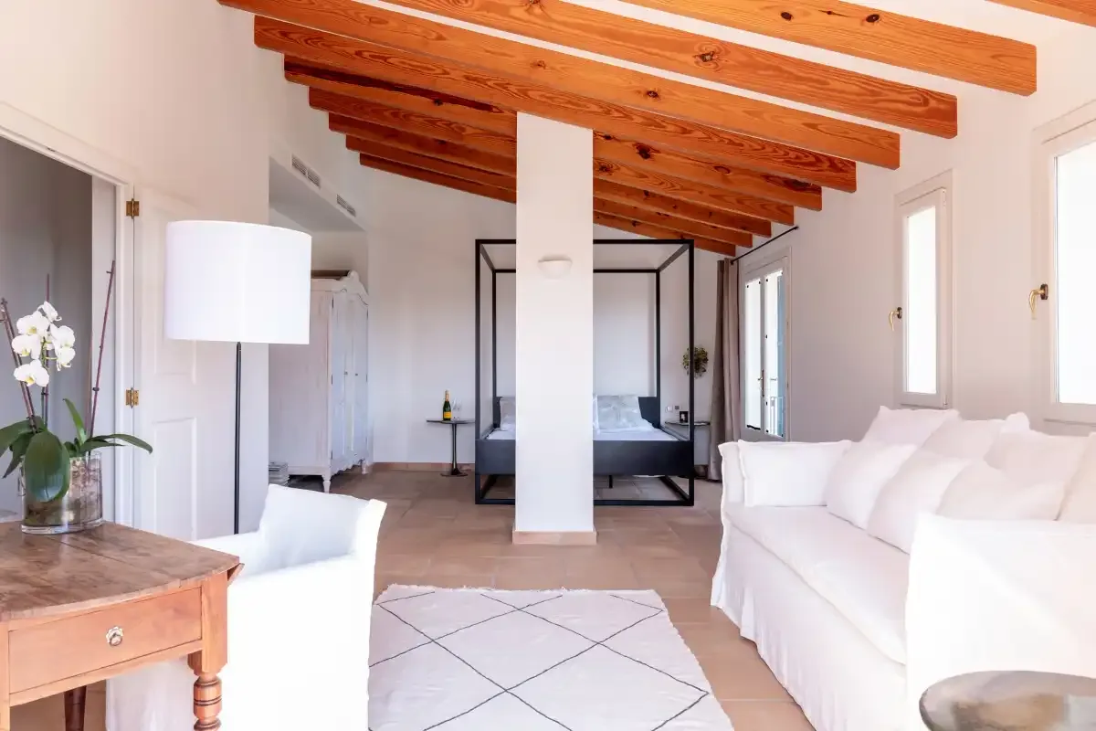 A bright living room with white seating and exposed wooden ceiling beams.