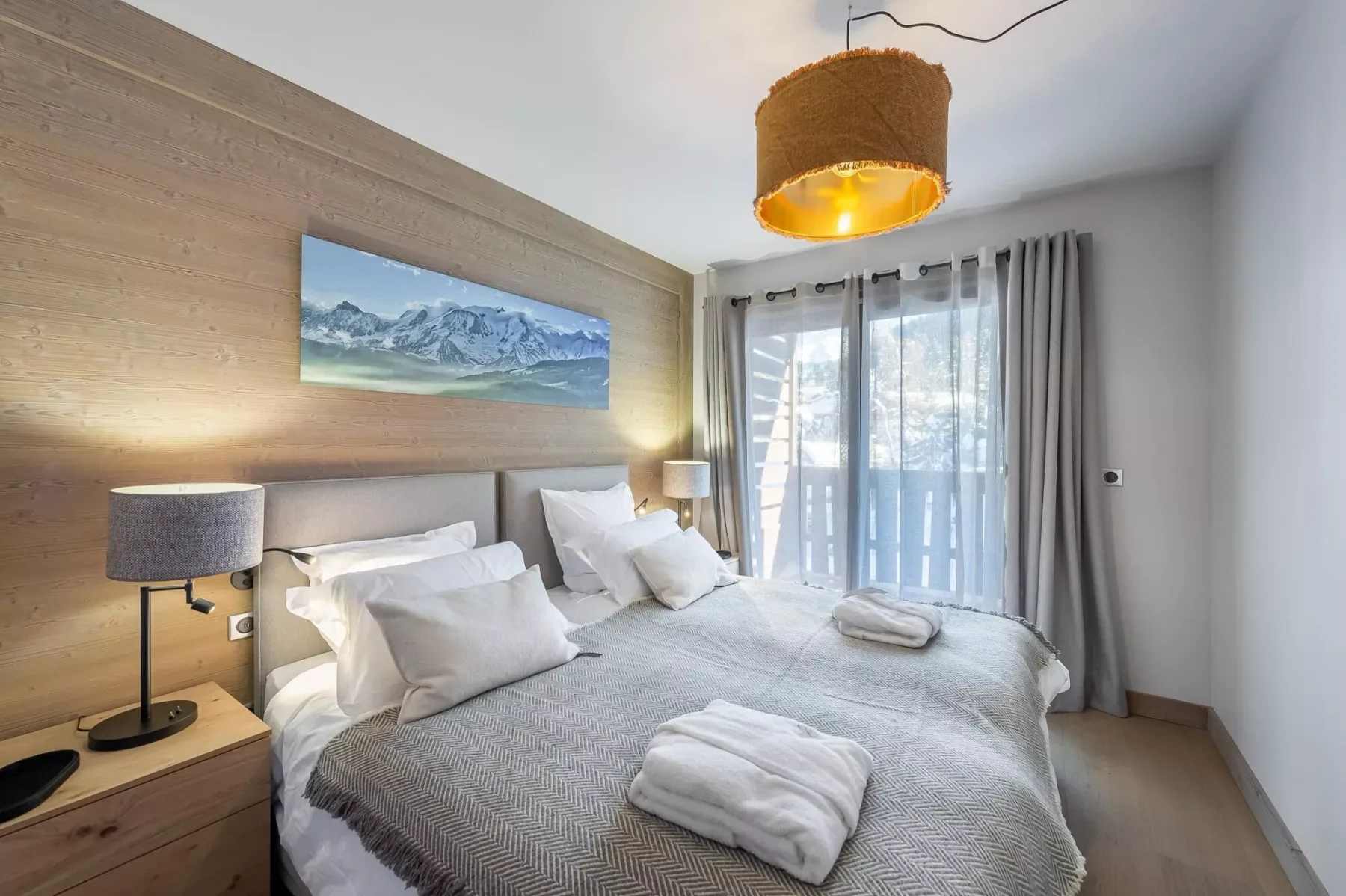 A bedroom with a large bed, bedside lamps, and curtains over glass doors.