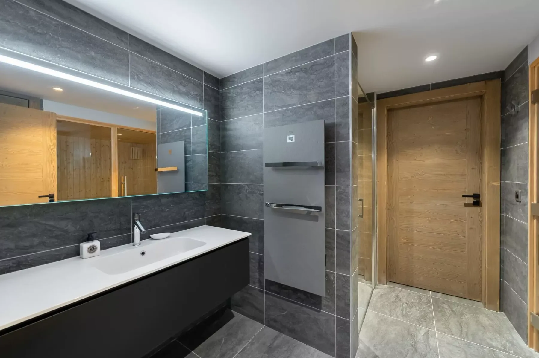 A modern bathroom with a wide sink counter and a wooden door.