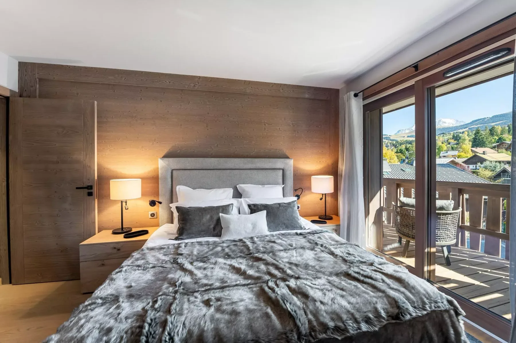 A bedroom with a bed beside large windows overlooking a mountain landscape.