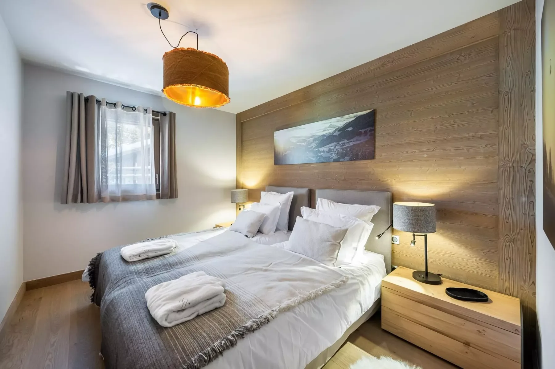 A bedroom with a double bed, white bedding, and a wood-paneled wall.