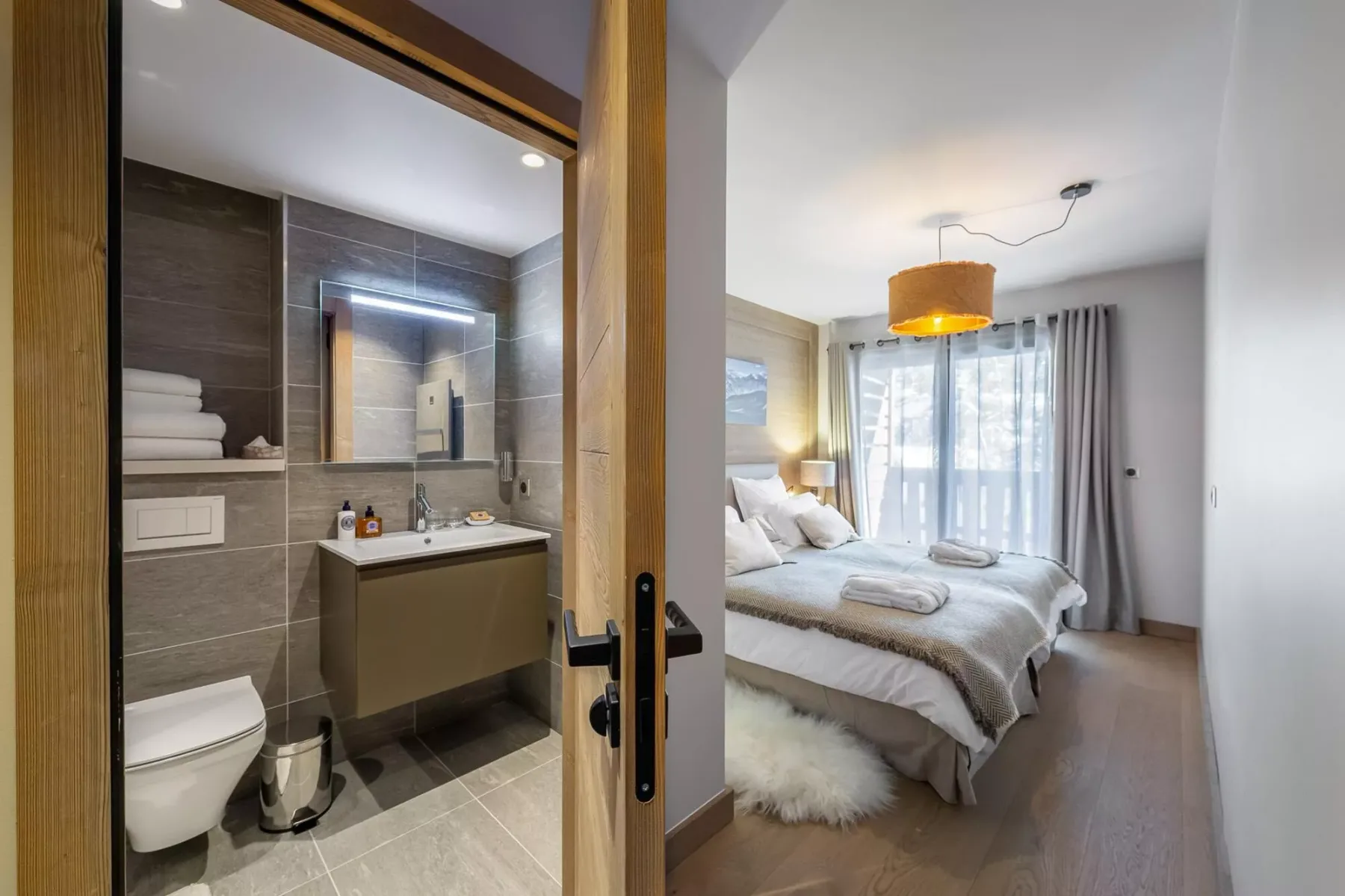 A bedroom with a neatly made bed and an adjoining bathroom visible through an open doorway.