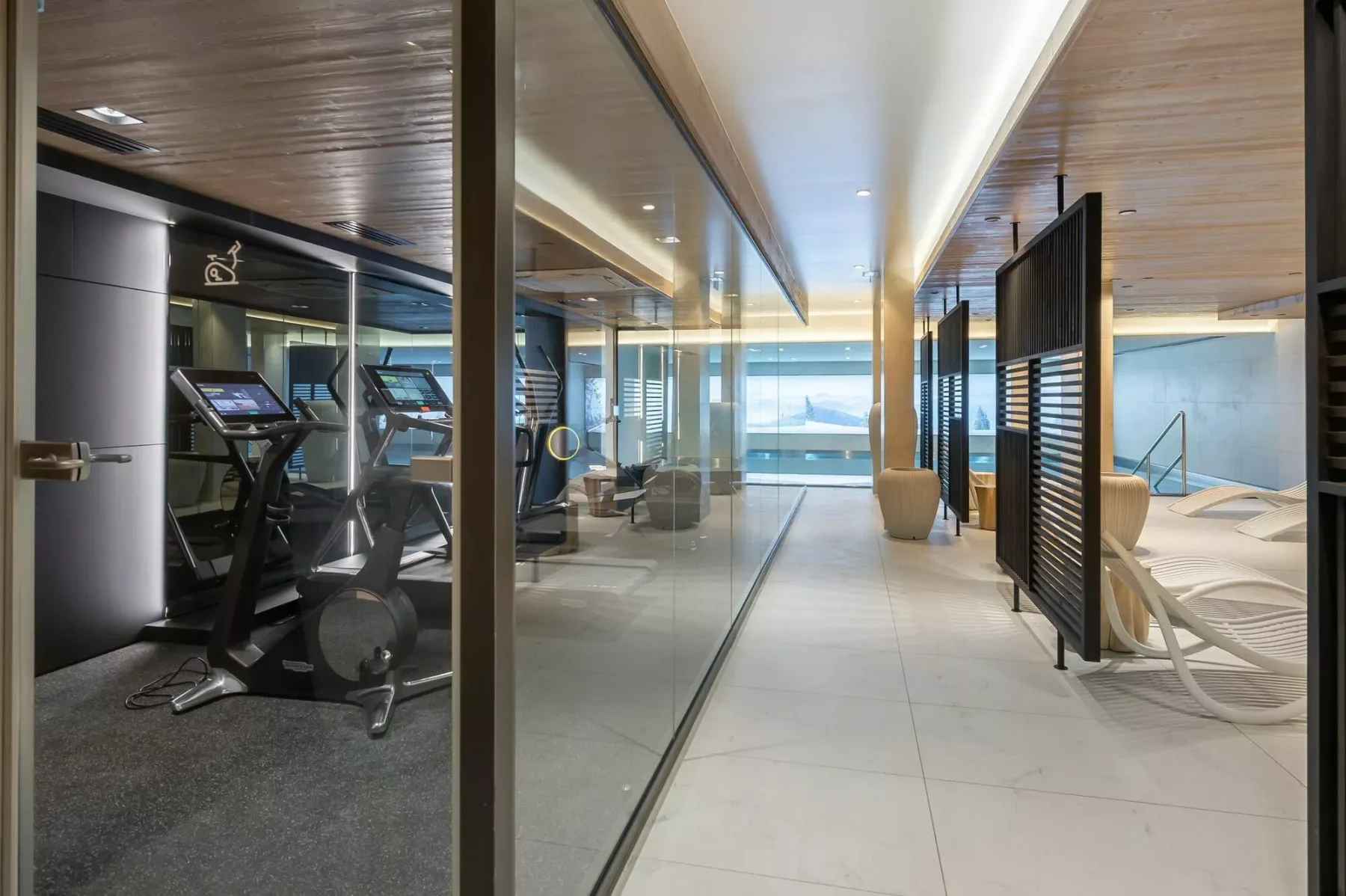 A modern indoor fitness and pool area with exercise equipment beside the swimming pool.