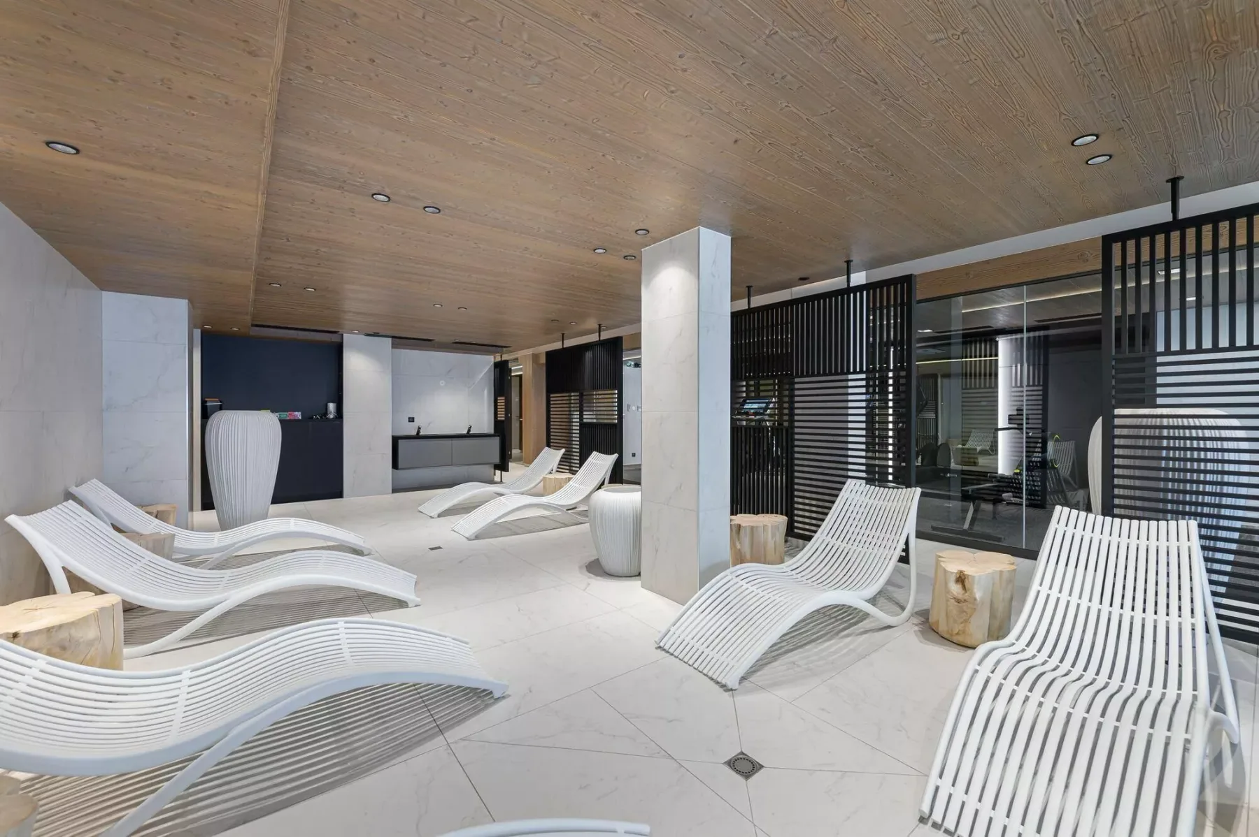 A modern indoor lounge with white reclining seating and dark slatted screens.