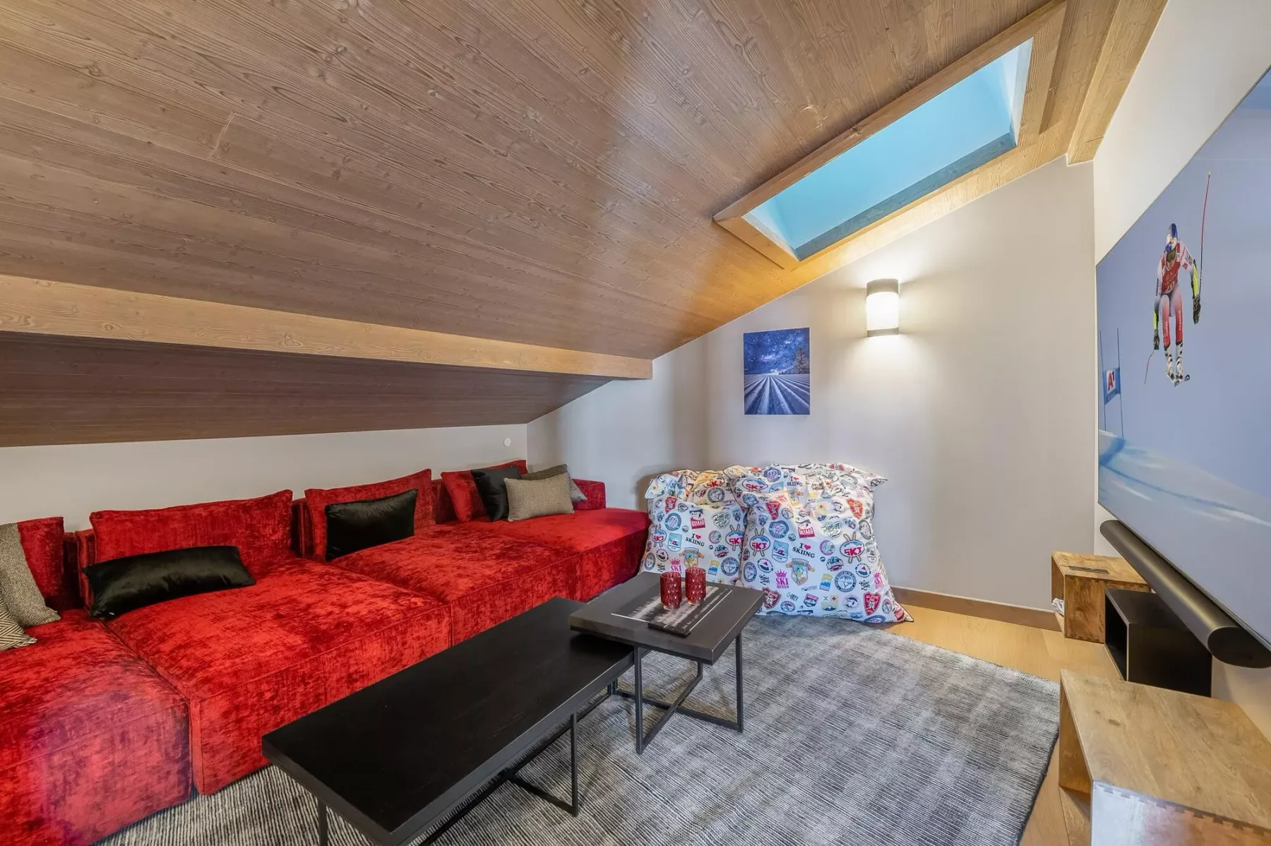 A living room with red seating, a coffee table, and a sloped wooden ceiling.