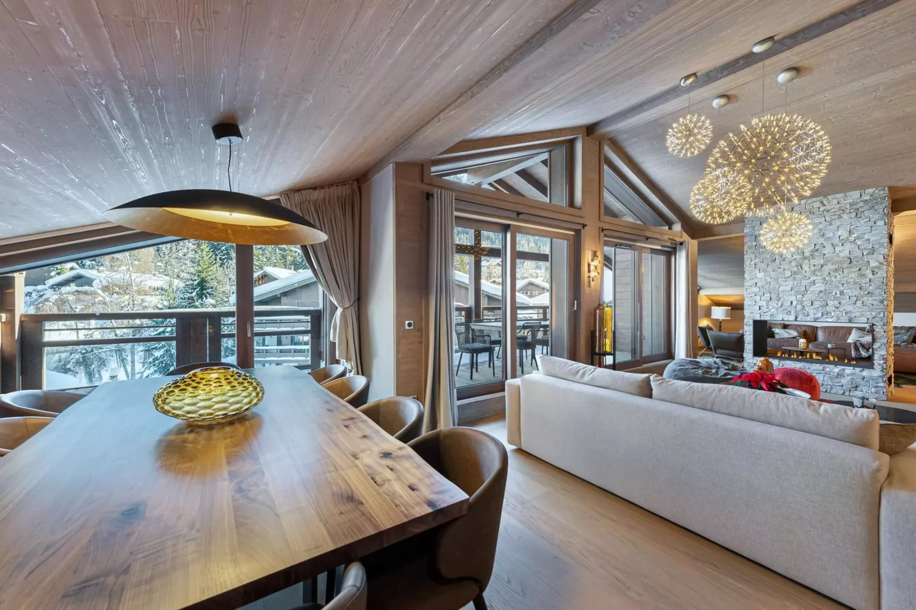 A dining and living area with a long wooden table, seating, and a stone fireplace.