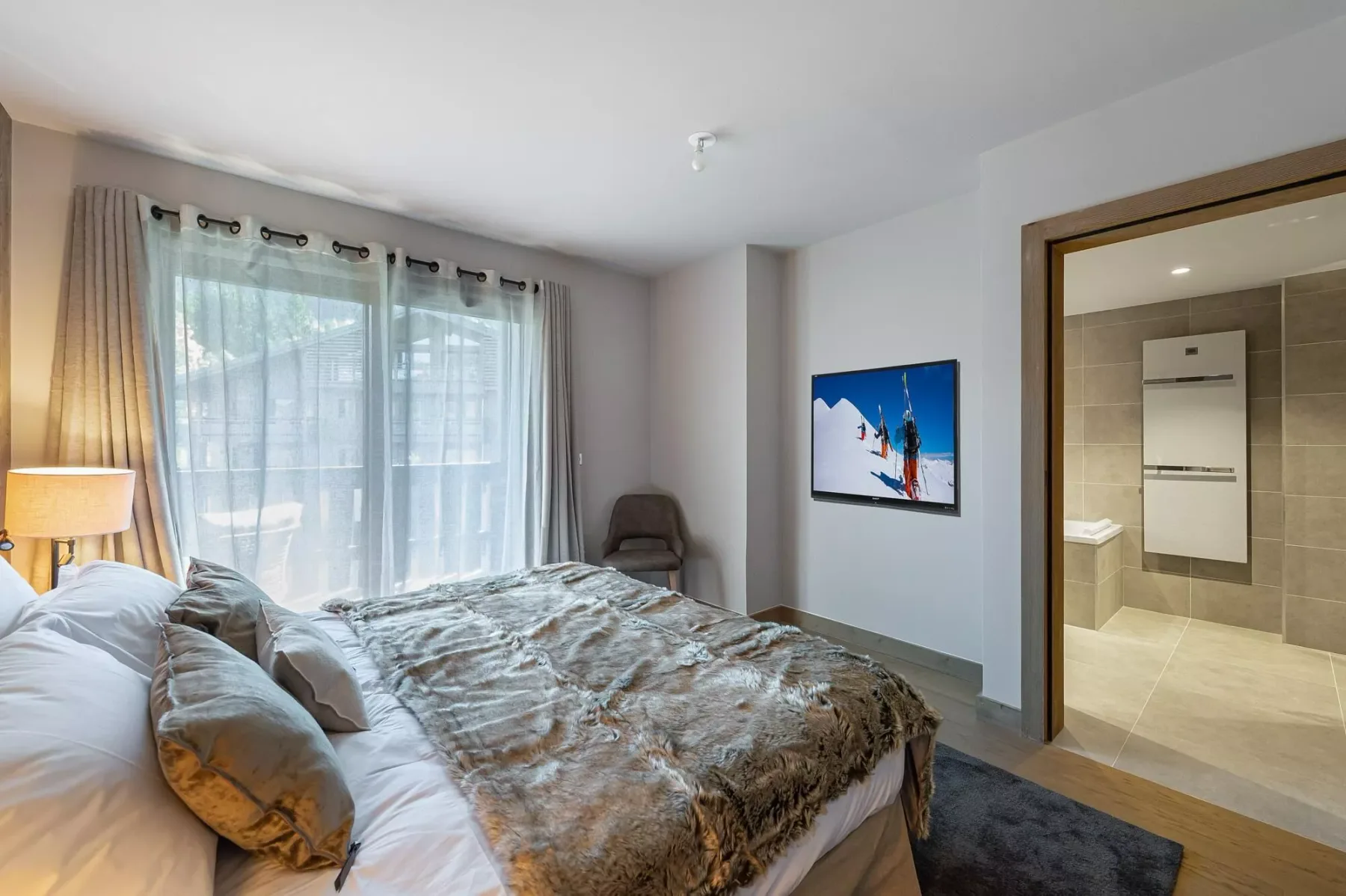 A bedroom with a large bed beside a window and an open bathroom doorway.